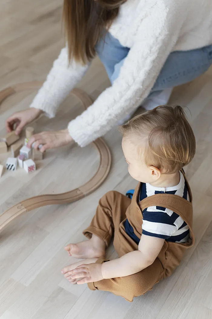 Un enfant et une femme jouent avec un train en bois sur le sol
